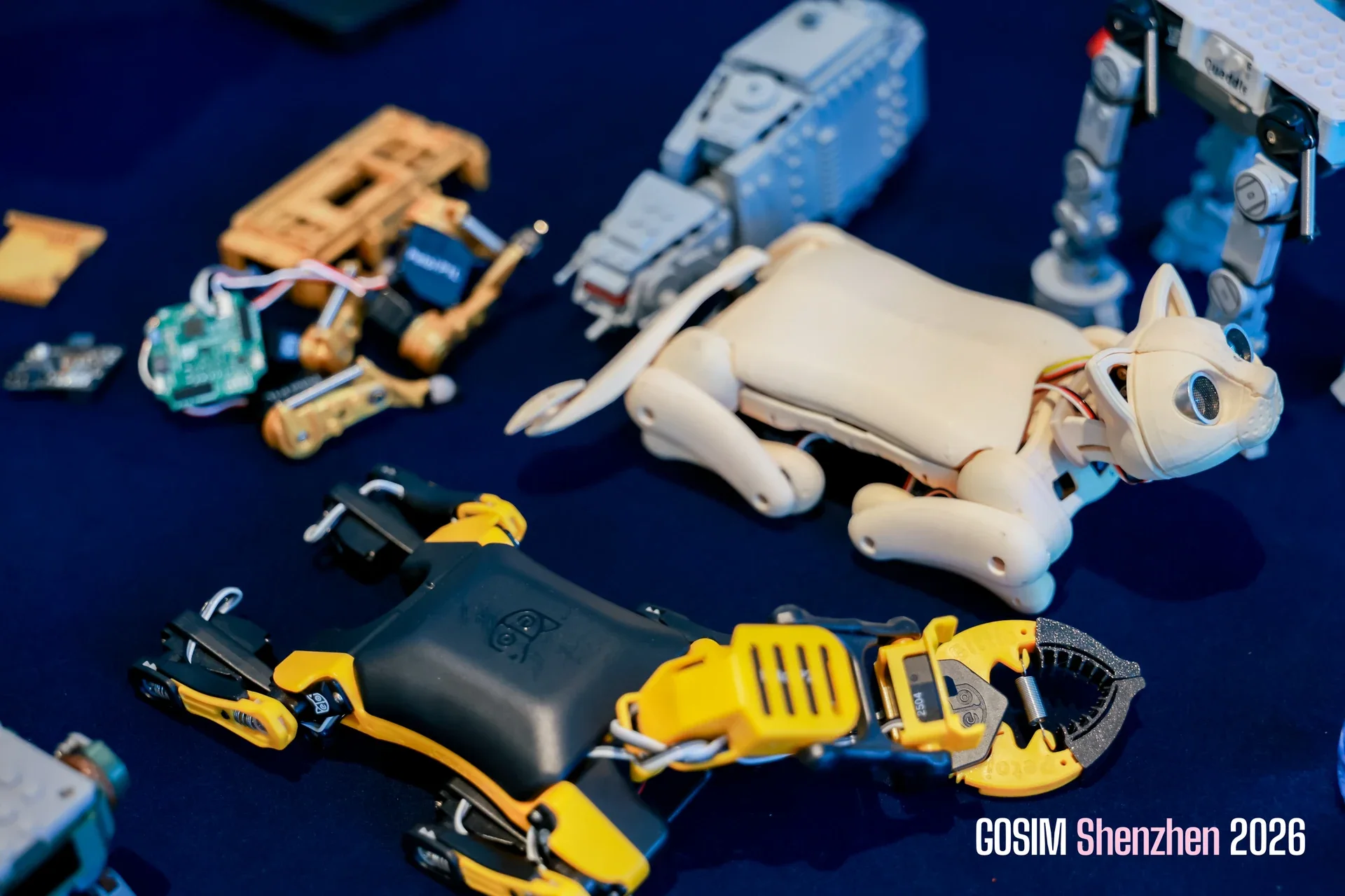 A cat-shaped robot and other small robotics projects displayed on a blue exhibition table